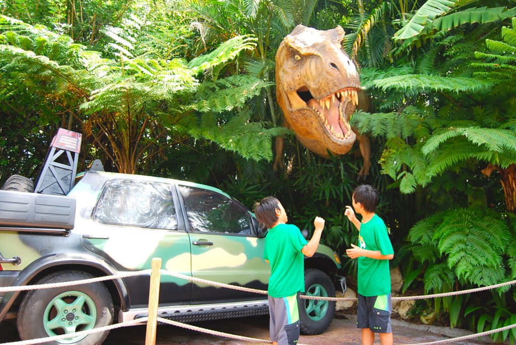 ジャングルの茂みから顔を出す恐竜に驚く子どもたち